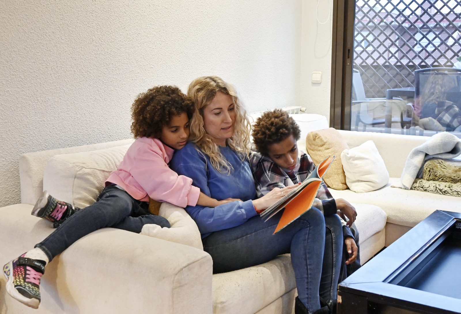 Người mẹ ngồi đọc sách cùng hai con trên ghế sofa.